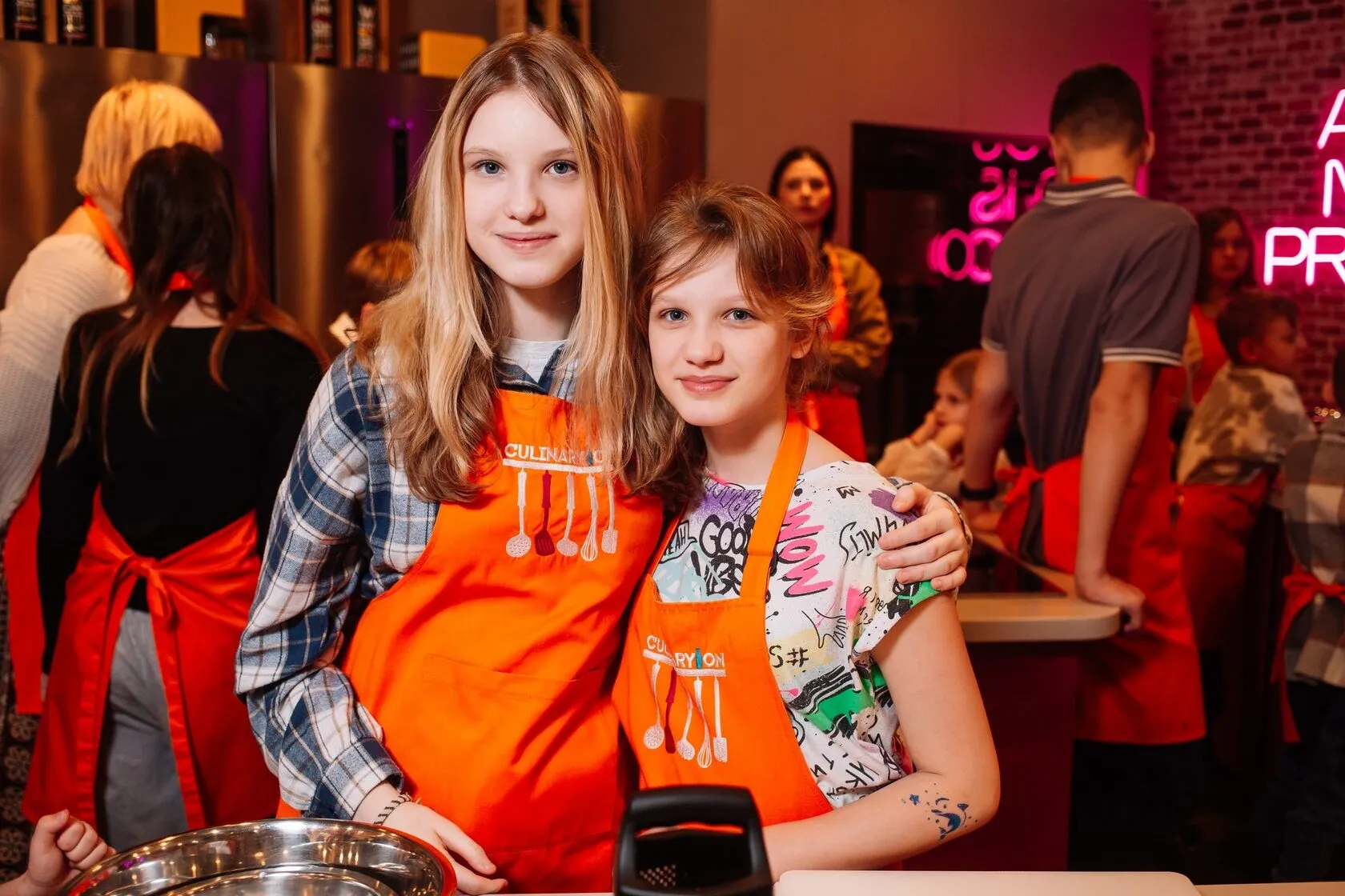 Мастер-класс по приготовлению пиццы для детей в CulinaryOn — две девочки позируют в оранжевых фартуках